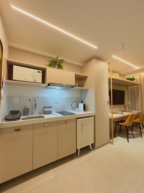 A modern kitchen with a built-in microwave, a sink, and a small refrigerator. There is a dining area with a table and chairs. - Beachfront Retreat: Premium Escape with Direct Beach Access (João Pessoa)