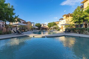 A swimming pool with lounge chairs and umbrellas, surrounded by buildings with balconies and trees. - Modern luxury & unforgettable sunsets at Mavila - huge patio w pool (Cabo San Lucas)