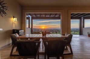 A dining area with a table and chairs, a wall-mounted light, and a view of the sunset. - Modern luxury & unforgettable sunsets at Mavila - huge patio w pool (Cabo San Lucas)