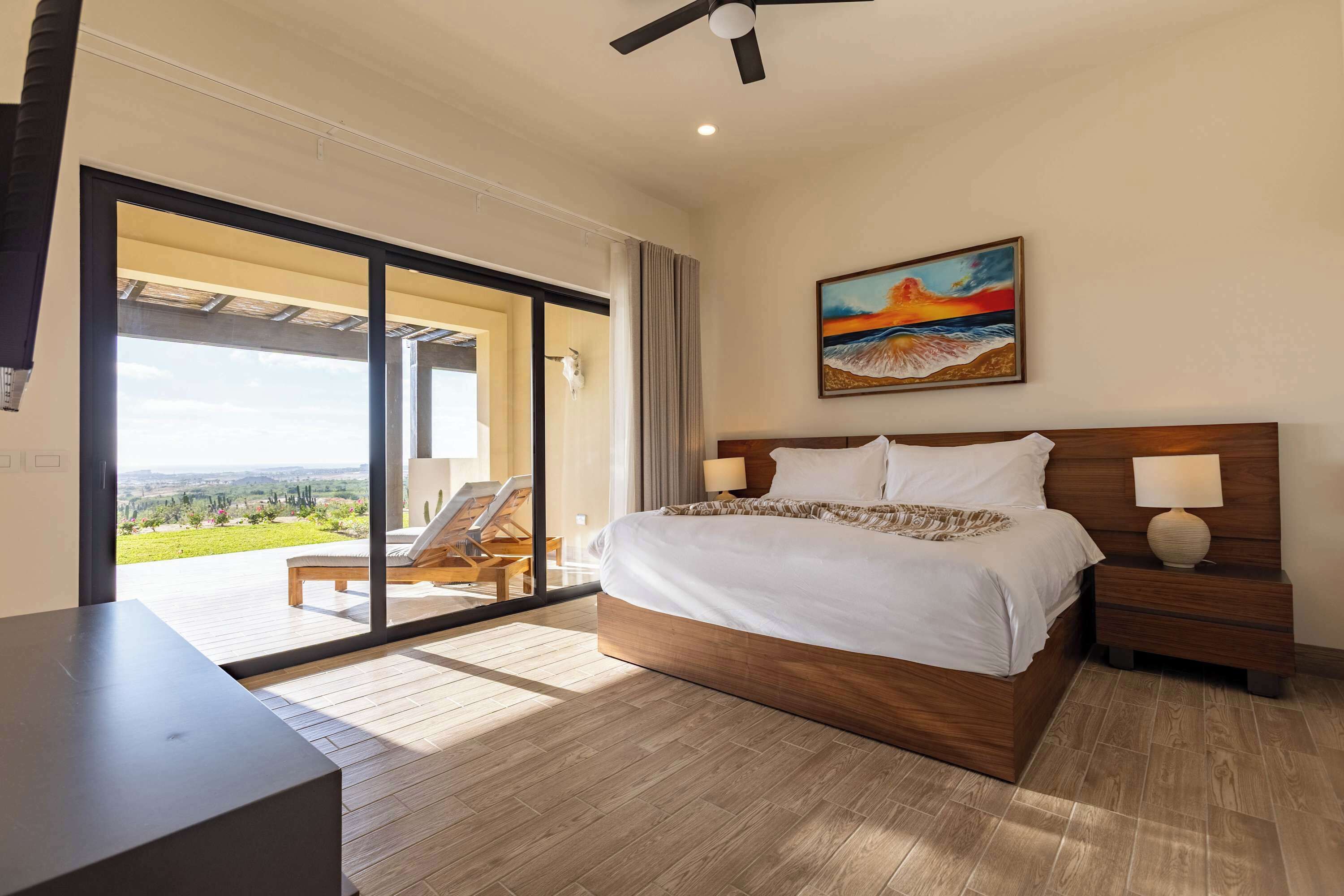 A bedroom with a large bed, two bedside lamps, a ceiling fan, and a painting.