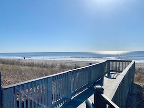Ein hölzerner Steg führt zu einem Strand mit freiem Blick auf das Meer.