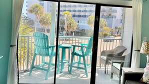 A room with a ceiling fan, a sliding glass door leading to an outdoor area with chairs, a sofa, and a table with a remote control. - Incredible Beach Villa 1bd/1ba Myrtle Beach (Myrtle Beach)