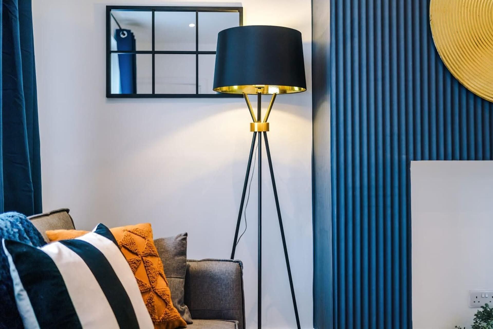 A modern living room with a floor lamp, a sofa with patterned cushions, and a decorative mirror on the wall.