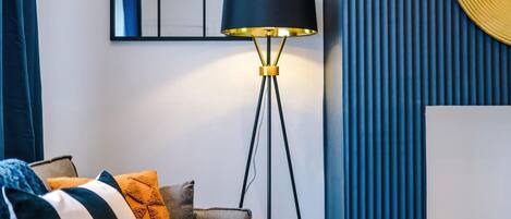 A modern living room with a floor lamp, a sofa with patterned cushions, and a decorative mirror on the wall.