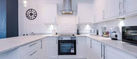 Una cocina moderna con armarios blancos, horno empotrado, campana extractora de acero inoxidable y un reloj de pared.