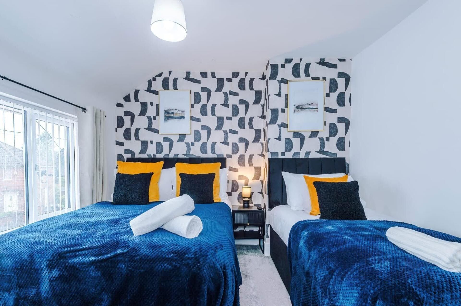 A hotel room with two beds, a patterned wall, and a window.