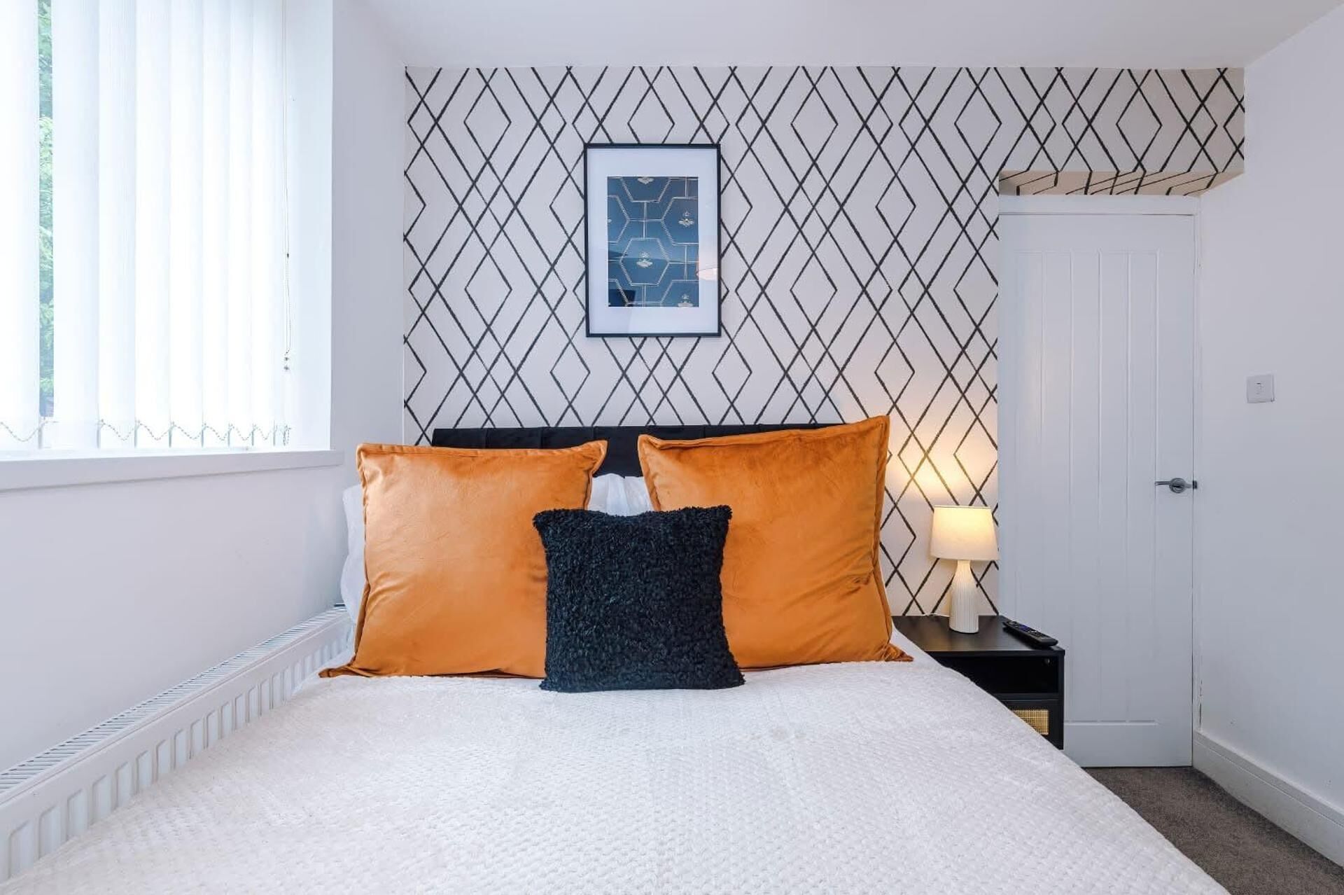 A bedroom with a bed, two pillows, a nightstand, a lamp, and a framed picture on the wall.