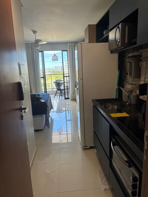 Eine Küche mit Kühlschrank, Backofen und Mikrowelle. Es gibt einen Essbereich mit Tisch und Stühlen. Vom Fenster aus ist ein Balkon mit Blick auf die Stadt zu sehen.