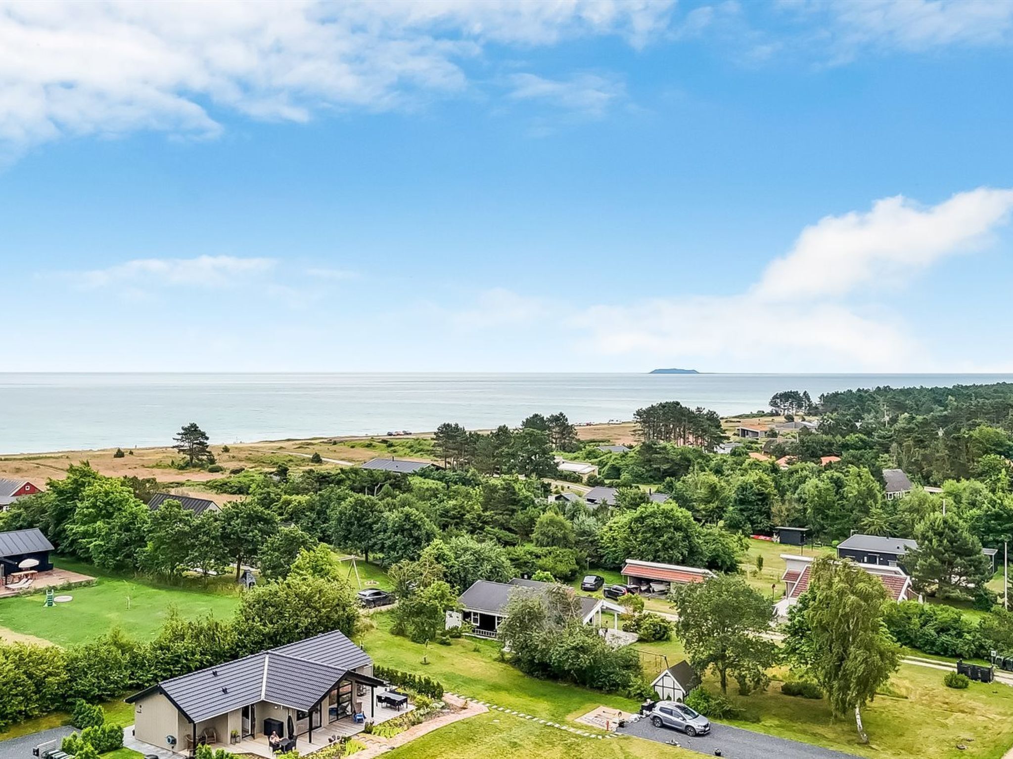 A residential area with houses, a grassy field, and a body of water in the background.
