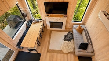 A cozy cabin interior with a wooden dining table, sofa, and a flat-screen TV.