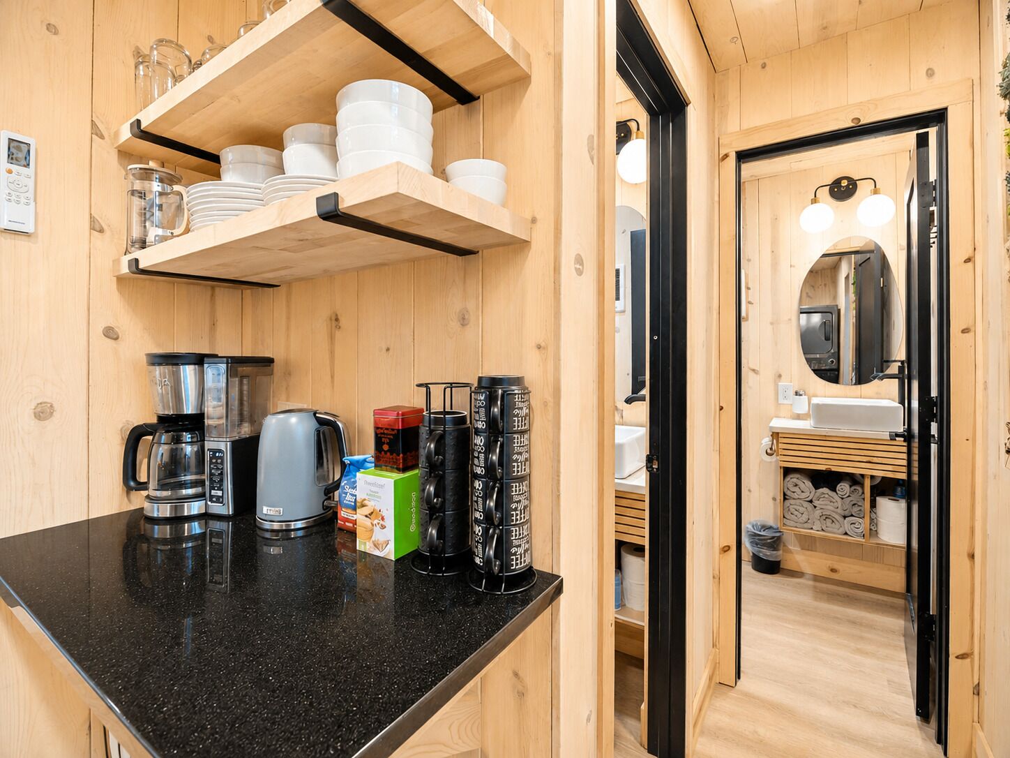 Cocina compacta con encimera negra, cafetera, hervidor y recipientes de almacenamiento.