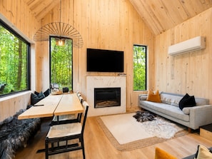 A modern interior with a wooden floor, a fireplace, a sofa, a dining table with chairs, and a TV mounted on the wall.