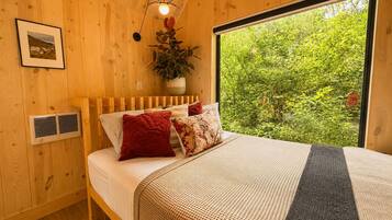 A wooden room with a bed, a window, and a plant.
