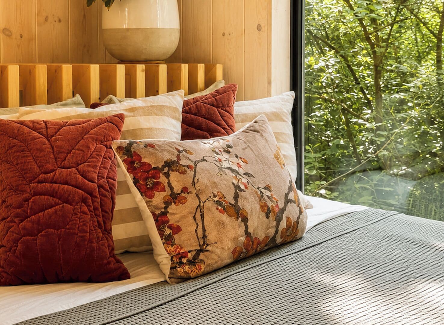 Un lit avec une tête de lit, plusieurs oreillers et une vue sur la verdure à l’extérieur.