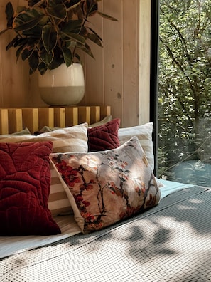 A bed with a striped pillow, a red pillow, and a floral pillow.