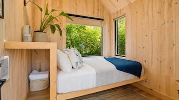 Ein Schlafzimmer mit einem Bett, einem Fenster, einer Pflanze und einem Regal mit Gegenständen.