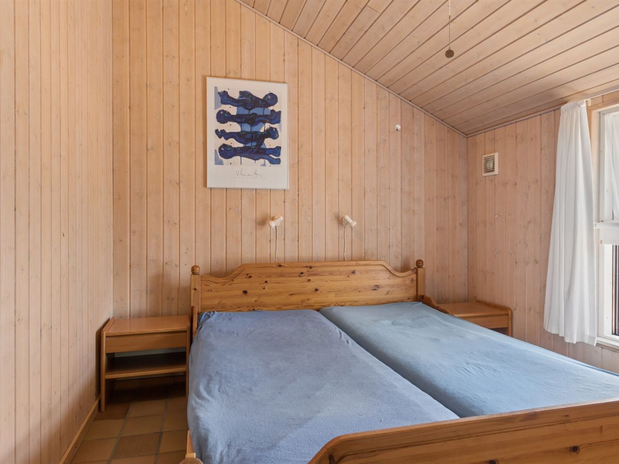 A wooden-paneled room with a bed, a nightstand, and a framed artwork on the wall.