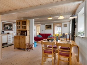 En hyggelig indretning med et træspisebord, stole, en rød sofa og et køkken med træskabe.