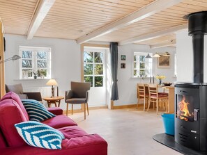 En hyggelig stue med en rød sofa, et spiseområde og en brændeovn.