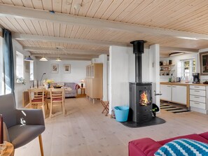 En moderne stue med central pejs, spiseområde og et køkken med træskabe og bordplade.