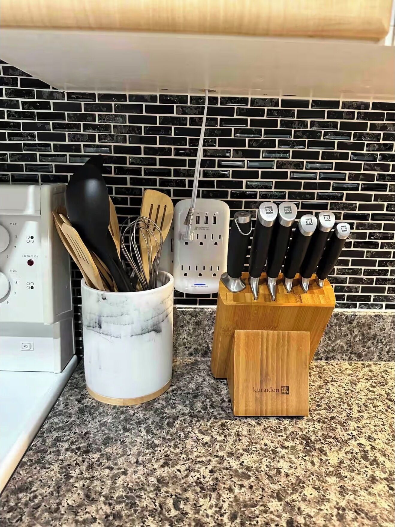 A kitchen counter with a marble container holding utensils, a knife block with knives, and a power strip.