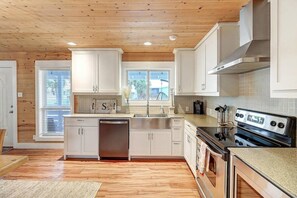 Una cocina con techo de madera, armarios blancos, electrodomésticos de acero inoxidable y una ventana.