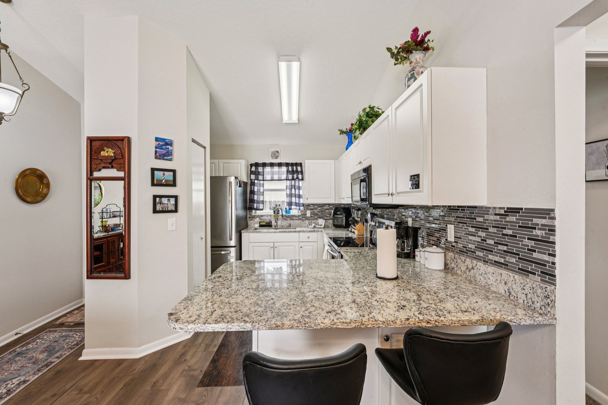 A kitchen with a granite countertop, white cabinets, a black backsplash, and a dining area with two chairs.