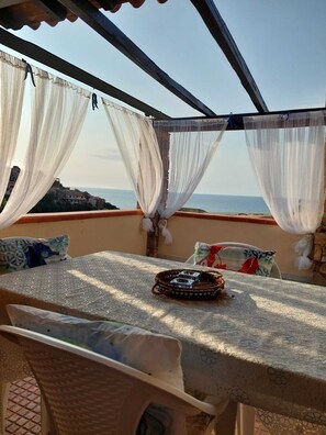Ein überdachter Außenbereich mit Tisch, Stühlen und Meerblick.