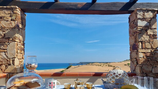 Mesa posta com comida e bebidas, um copo d'água e vista para a praia.