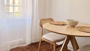 Una habitación con una mesa redonda de madera, dos sillas, un aire acondicionado blanco y una ventana con vistas a edificios.