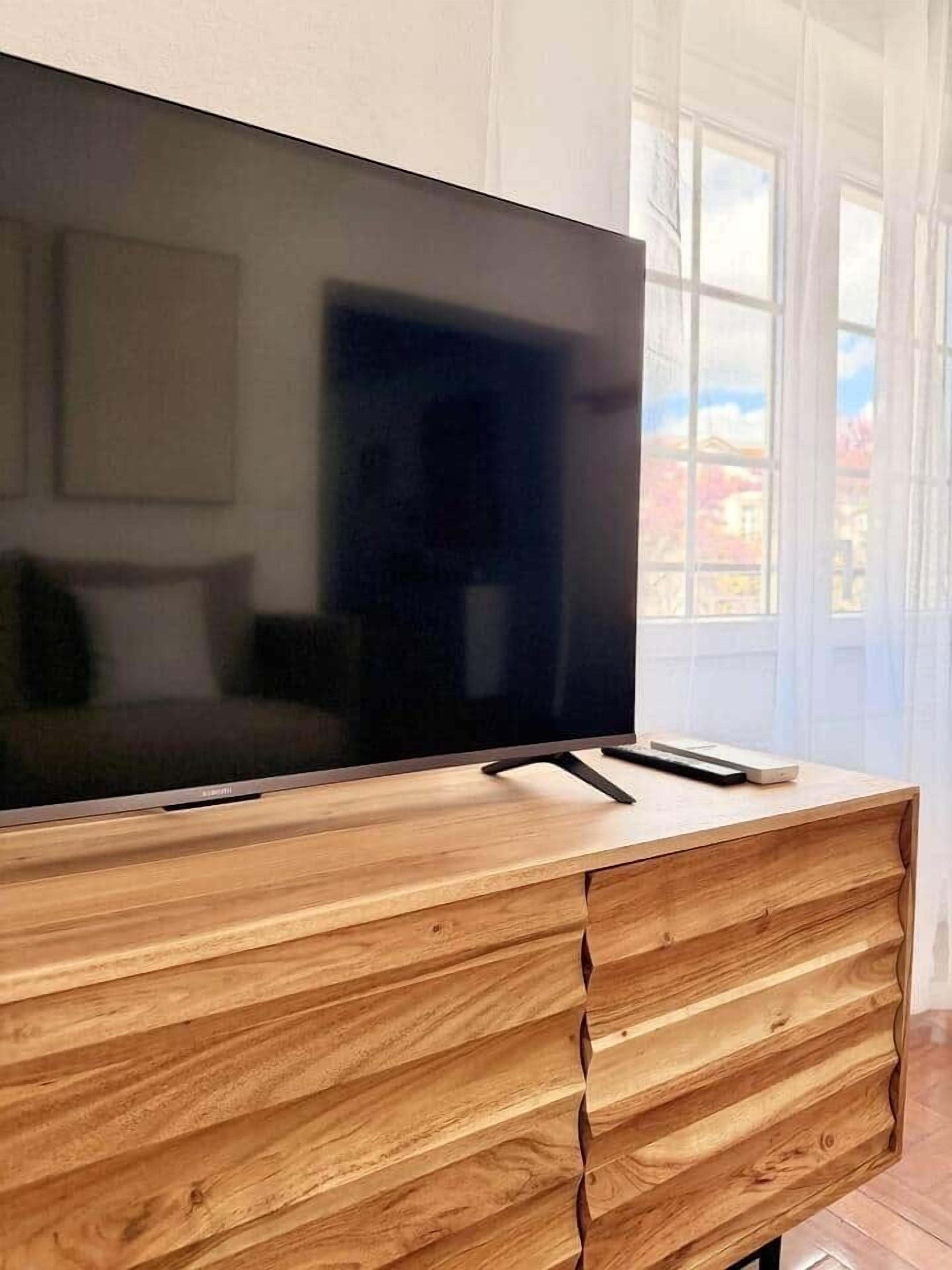 En platt-TV placerad på ett träskåp med en låda, en fjärrkontroll och en liten apparat på skåpets yta.
