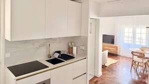 Una cocina moderna con armarios blancos, encimera negra y comedor con mesa y sillas de madera.