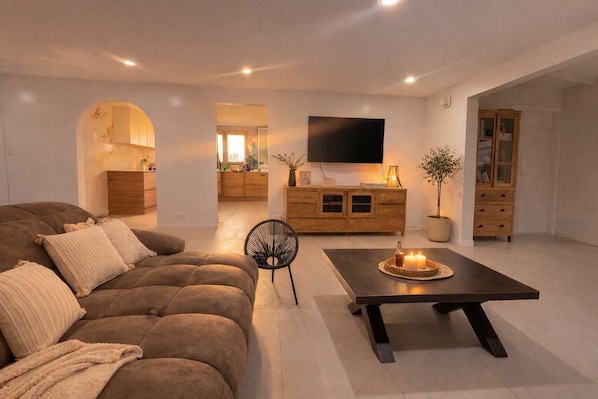 A modern living room with a sofa, a dining table, and a TV. - Spacious 5BR Villa w/ Pool Peaceful Authentic Aruba Stay Groups&Family Sleeps 10 (Santa Cruz)