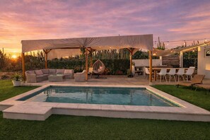 Une piscine dotée d’un espace détente couvert, de mobilier d’extérieur et offrant une vue sur le coucher de soleil.