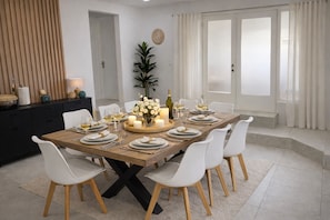 Comedor con una mesa de madera dispuesta para seis personas, sillas blancas, un florero, velas y una botella de vino.