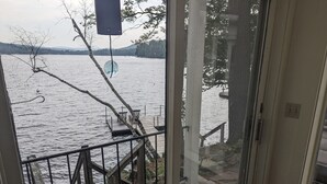 Uitzicht vanuit een kamer met een raam op een meer, een houten terras en een stoel.