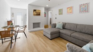 A modern living room with a sectional sofa, a dining table with chairs, a fireplace, and artwork on the walls. - Unit A.Stylish Hidden Gem-3 miles Beach & old Naples in Us41/2bedroom 1 bathroom (Naples)