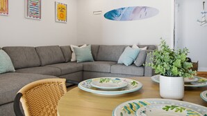 A modern living room with a gray sectional sofa, a wooden dining table with plates, a wicker chair, and a potted plant. - Unit A.Stylish Hidden Gem-3 miles Beach & old Naples in Us41/2bedroom 1 bathroom (Naples)
