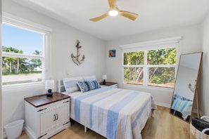 Ein Schlafzimmer mit Bett, Nachttischen, Deckenventilator, Fenster, Wanddekoration und Spiegel.
