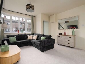 A modern living room with a sectional sofa, a round coffee table, a white dresser, and a large mirror with a neon sign. - Luxury & Affordable newly renovated for long stays (North East Lincolnshire)