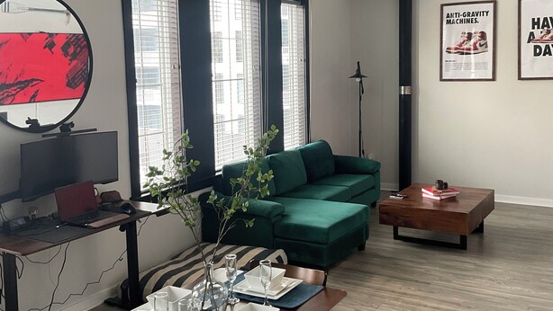 A modern living room with a green sofa, a dining table set for four, a TV, and large windows with blinds. - Industrial Tech Loft in Atlanta (Atlanta)