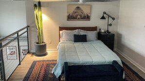 A bedroom with a bed, a nightstand, a lamp, a potted plant, a wall-mounted artwork, a staircase, and a railing. - Industrial Tech Loft in Atlanta (Atlanta)