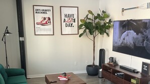 A living room with a green sofa, a coffee table, a potted plant, a TV, and two framed posters on the wall. - Industrial Tech Loft in Atlanta (Atlanta)