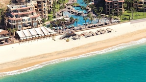 Luftaufnahme eines Hotels direkt am Strand mit mehreren Schwimmbecken, Strandliegen und einem Sandstrand.