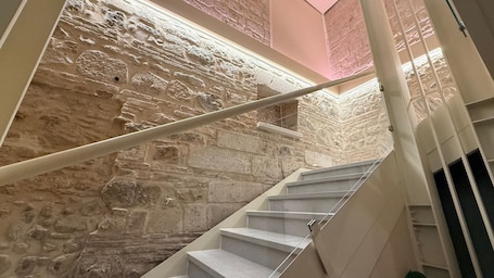 A staircase with a stone wall backdrop, a handrail, and a view of the upper floor.