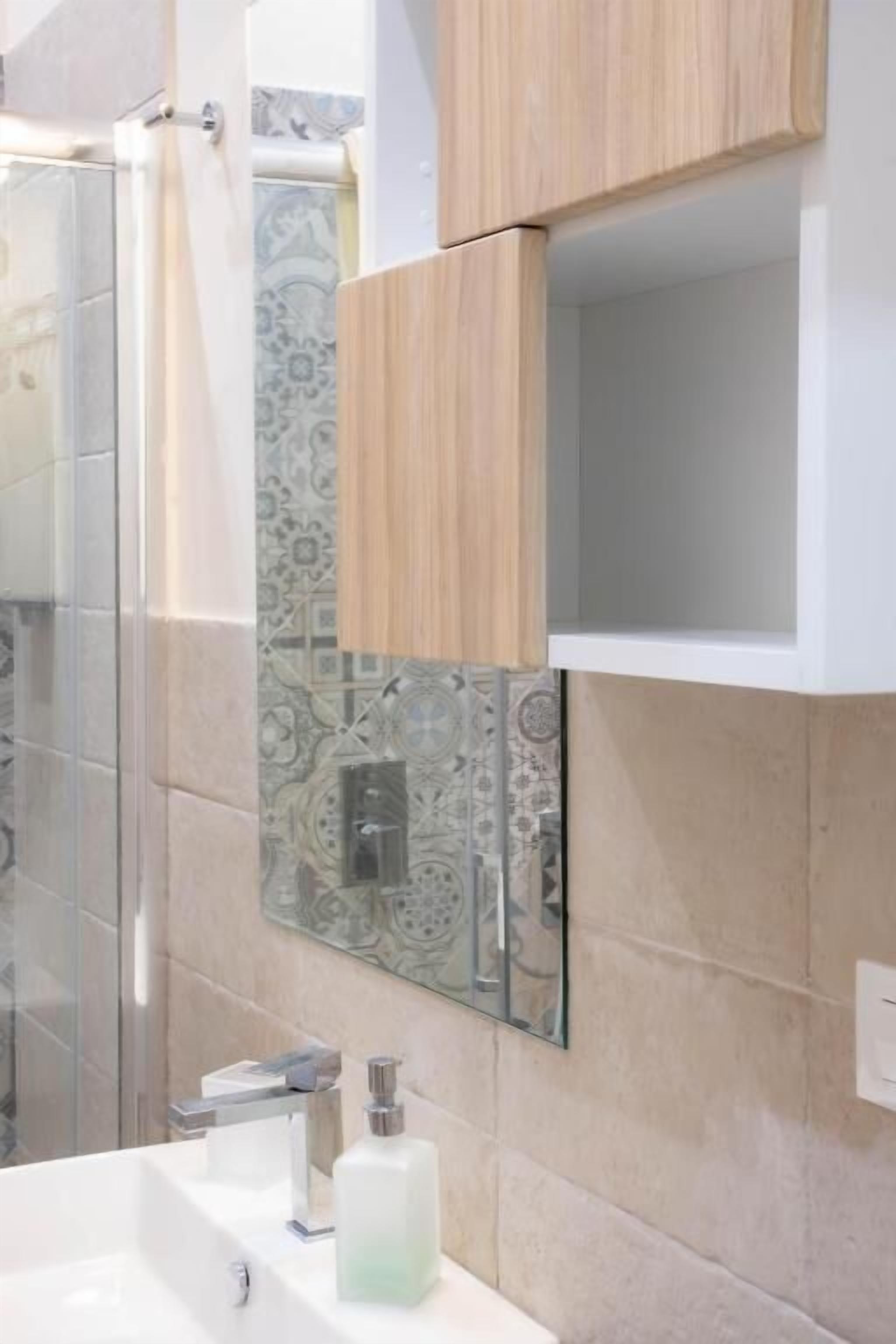 A bathroom with a shower, a sink with a mirror, and patterned tiles on the wall.