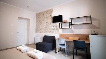 Un dormitorio con cama, escritorio, silla, televisor y pared de piedra.