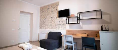 A bedroom with a bed, a desk, a chair, a television, and a stone wall.