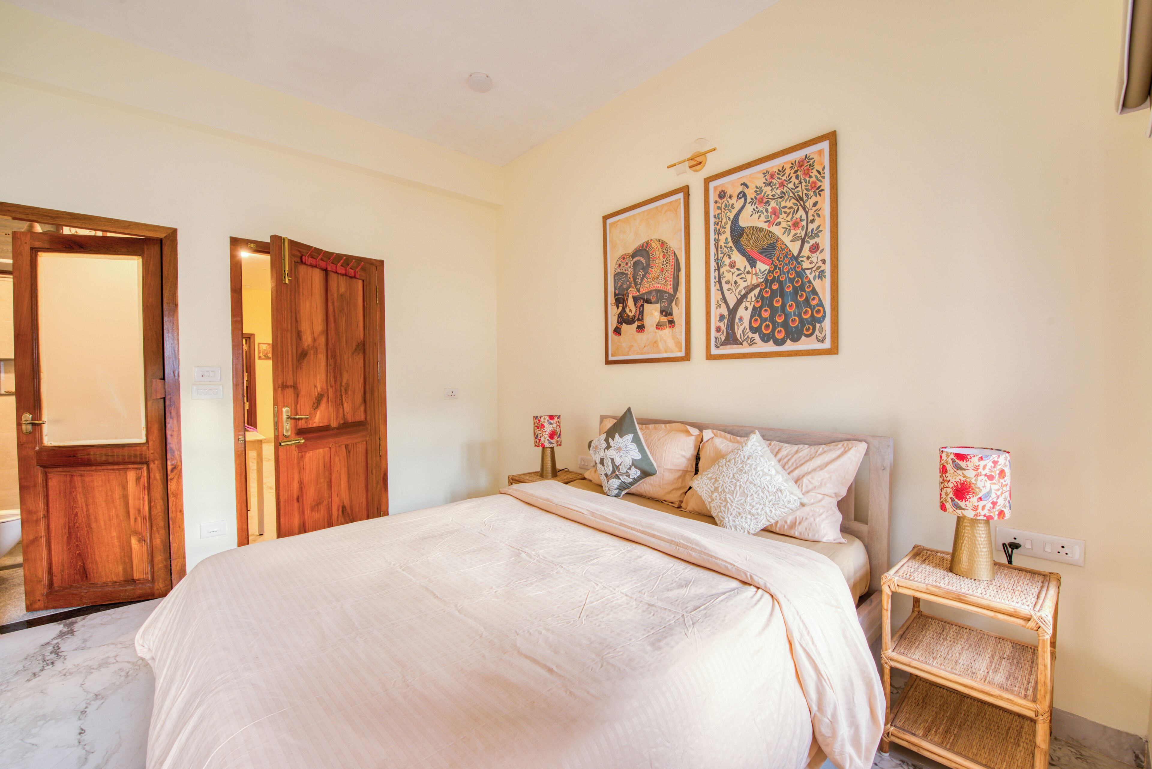 Une chambre à coucher avec un lit, des portes en bois, une table de chevet avec une lampe et deux tableaux accrochés au mur.