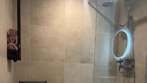Un baño moderno con ducha envuelta en vidrio, un perchero con toallas y una zona de lavamanos minimalista.